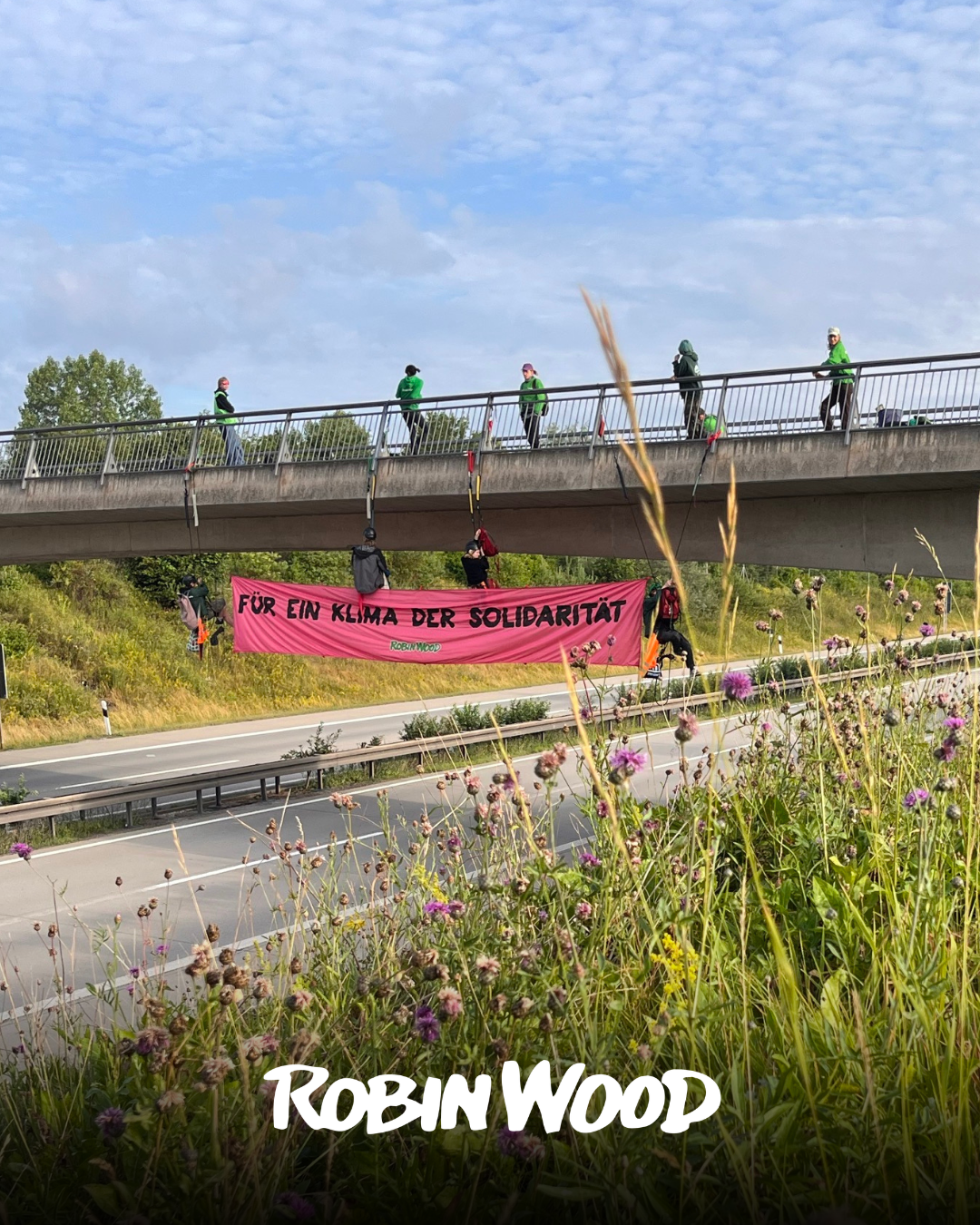 Aktivst*innen haben sich von einer Brücke über der A71 nach Erfurt abgeseilt und ein pinkes Banner mit der Aufschrift "Für ein Klima der Solidarität" zwischen sich gespannt.